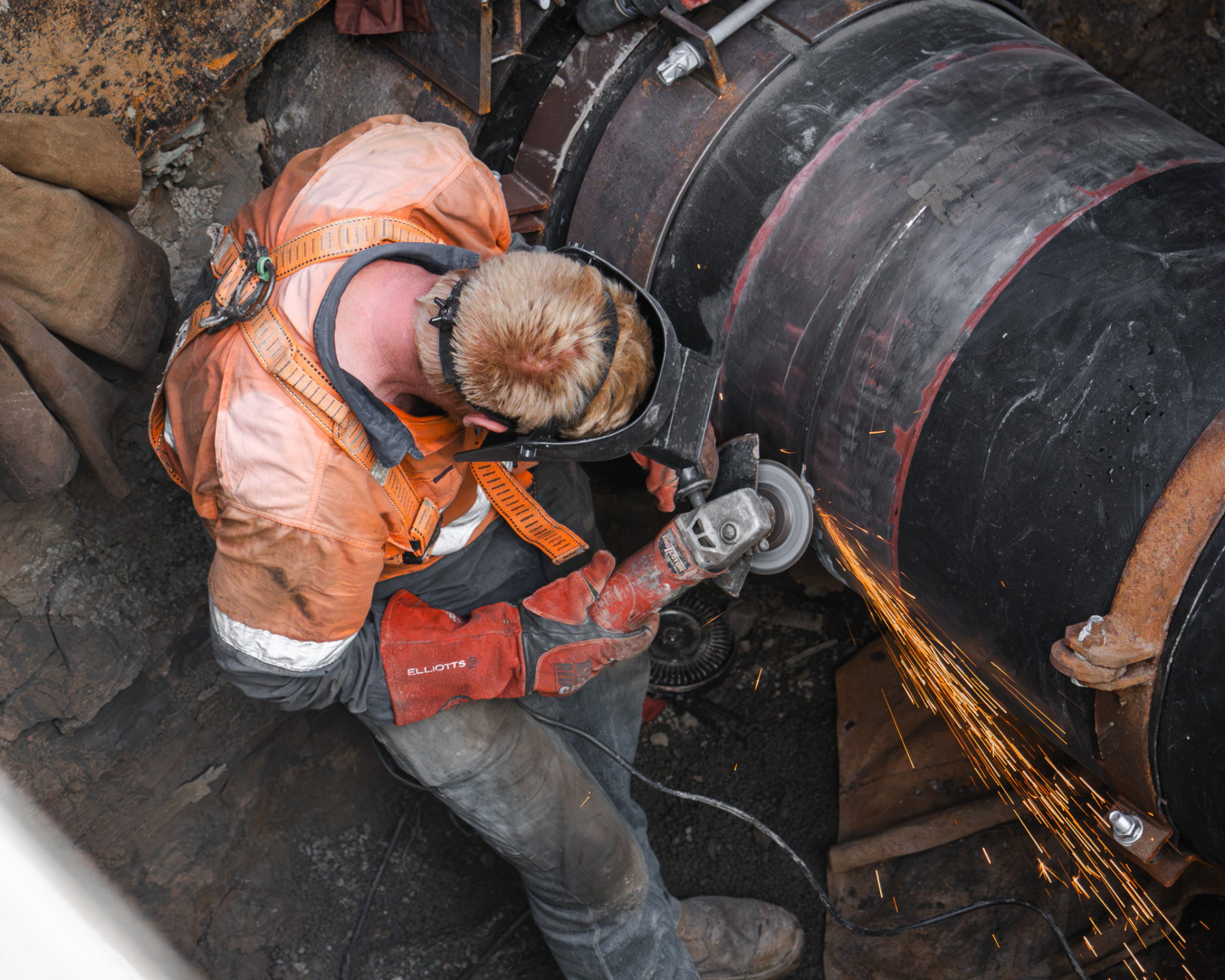 Tradesperson grinding a large steel pipeline