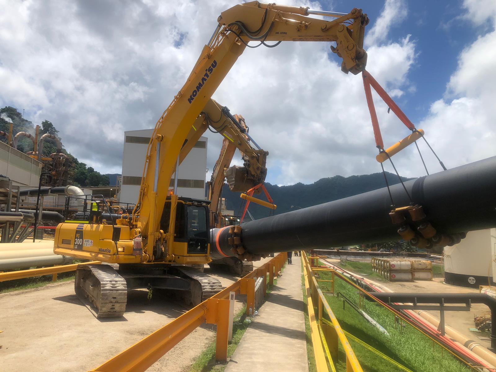Excavator lifting a large pipeline section at an industrial site