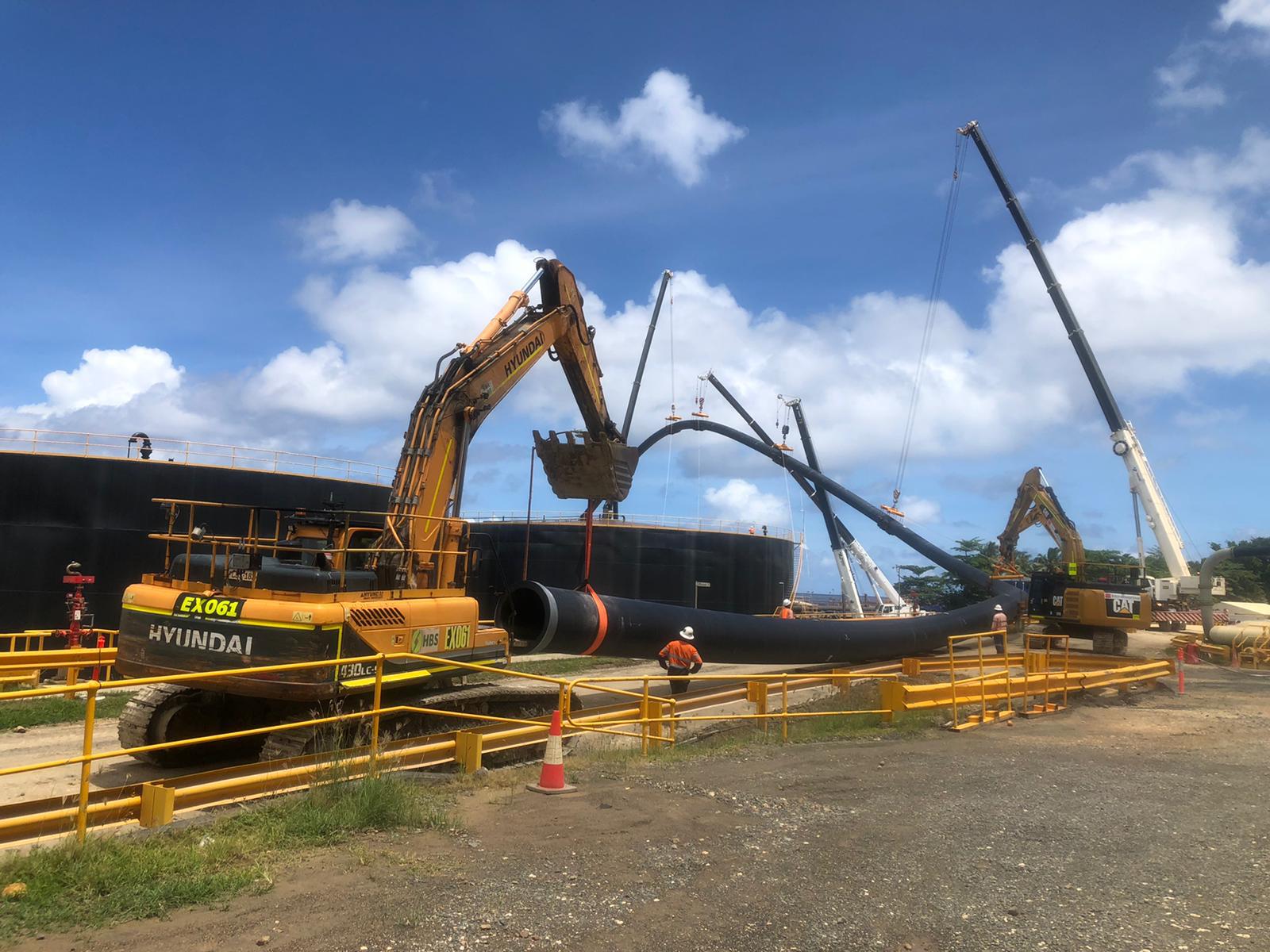 Excavators and cranes positioning large pipeline sections