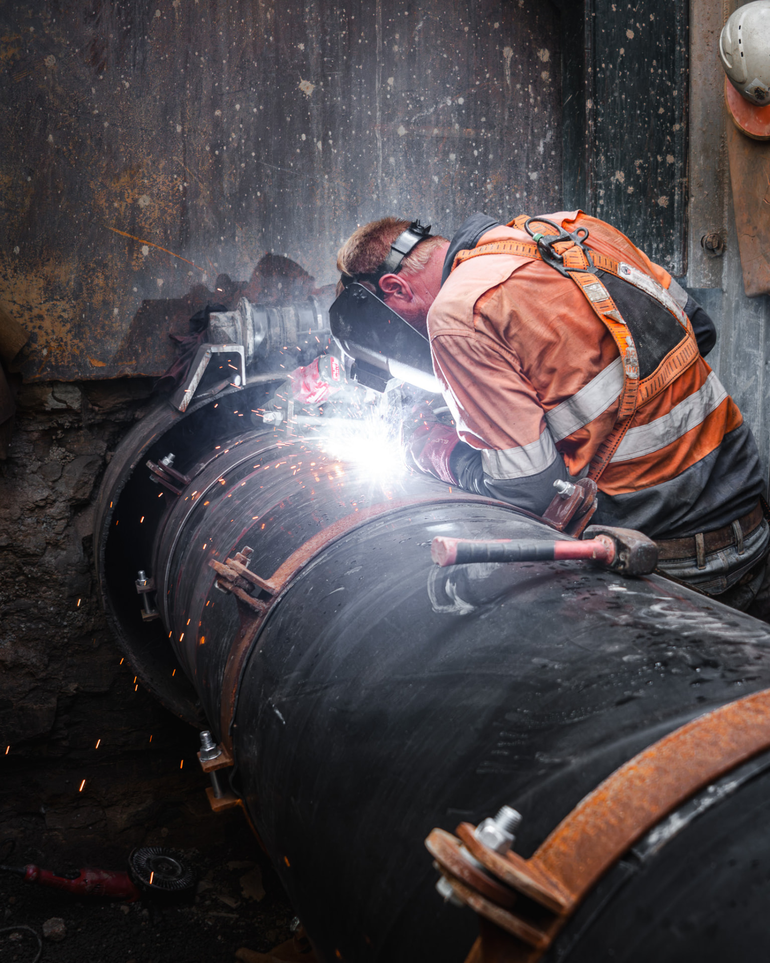 Welder in high-visibility workwear welding a large pipeline on site