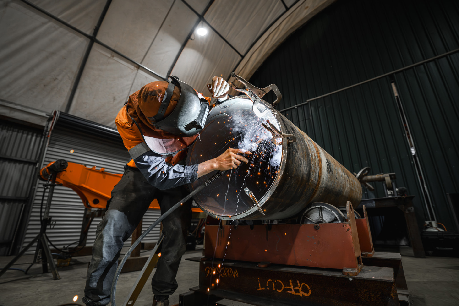 MXB Group welder in protective gear welding a large steel pipe with sparks flying in the Hemmant workshop